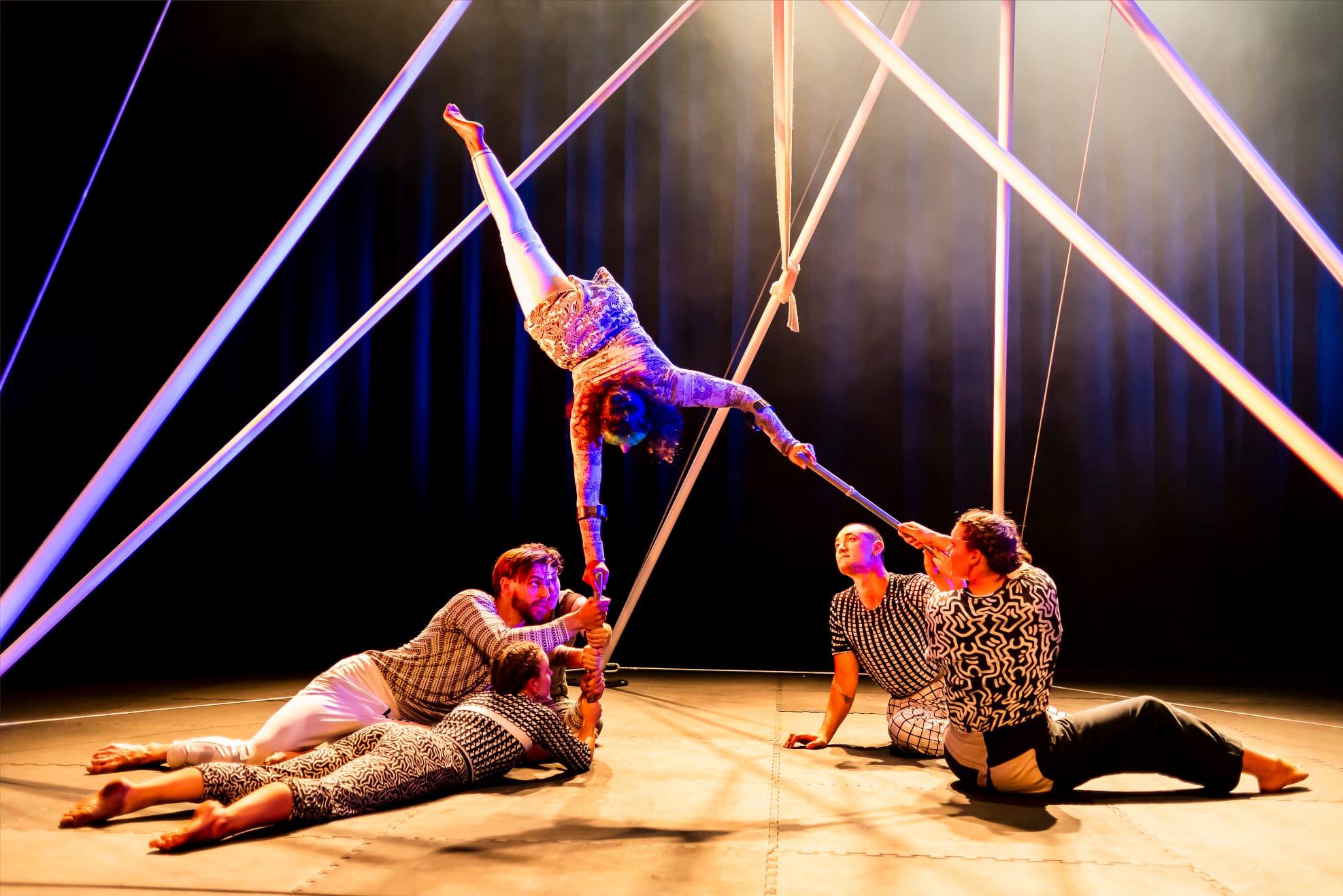 A performer dressed in a grey costume uses crutches to complete a handstand.